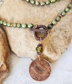 Irish coin pendant green pearl necklace on rock close up