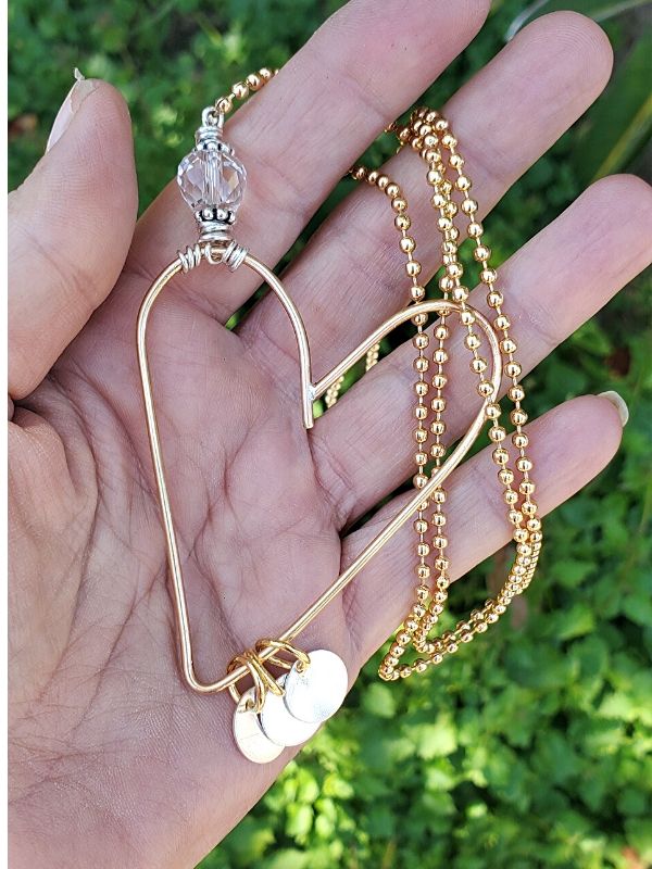 heart necklace on hand with green plants